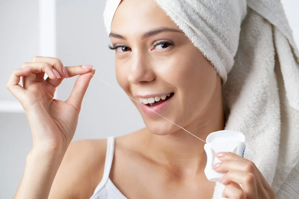 Giovane donna che usa uno stuzzicadenti e il filo interdentale per pulire i denti